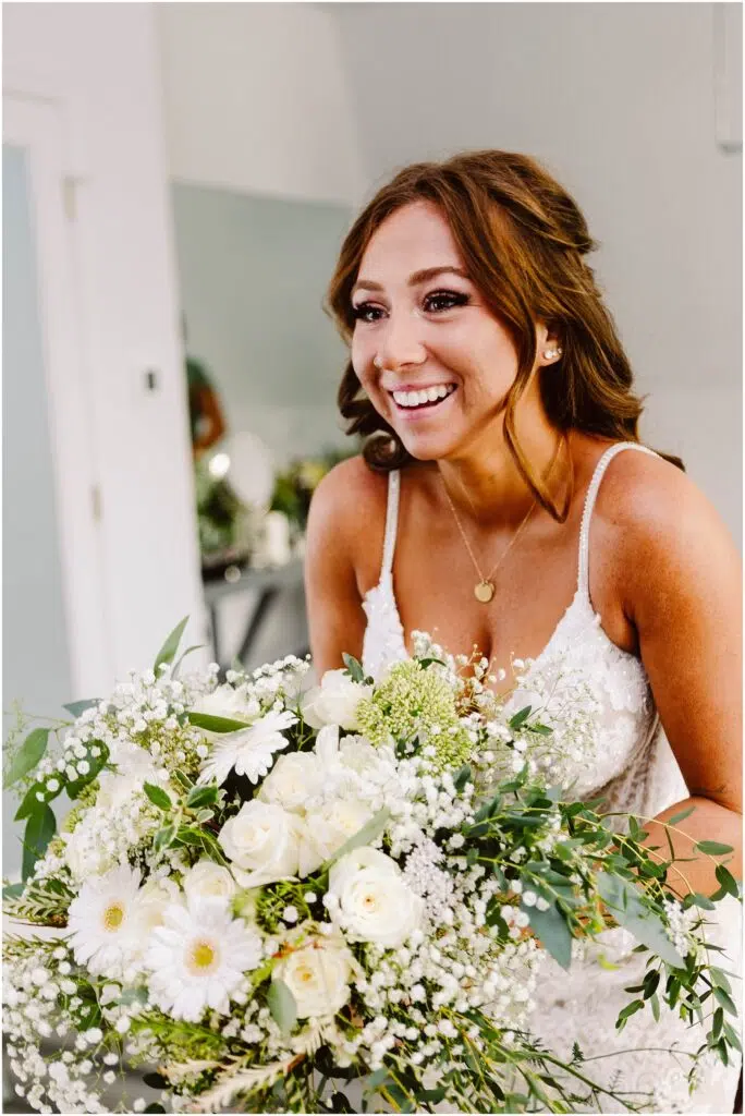 Snohomish Wedding Photographer GSquared Weddings A smiling bride with long brown hair holds a large bouquet of white flowers and greenery She is wearing a white lace dress with thin straps and a gold necklace The background is softly blurred focusing on the brides joyful expression Serving Seattle Snohomish and Washington State Snohomish Wedding Photographer GSquared Weddings A smiling bride with long brown hair holds a large bouquet of white flowers and greenery. She is wearing a white lace dress with thin straps and a gold necklace. The background is softly blurred, focusing on the brides joyful expression. Serving Seattle, Snohomish and Washington State