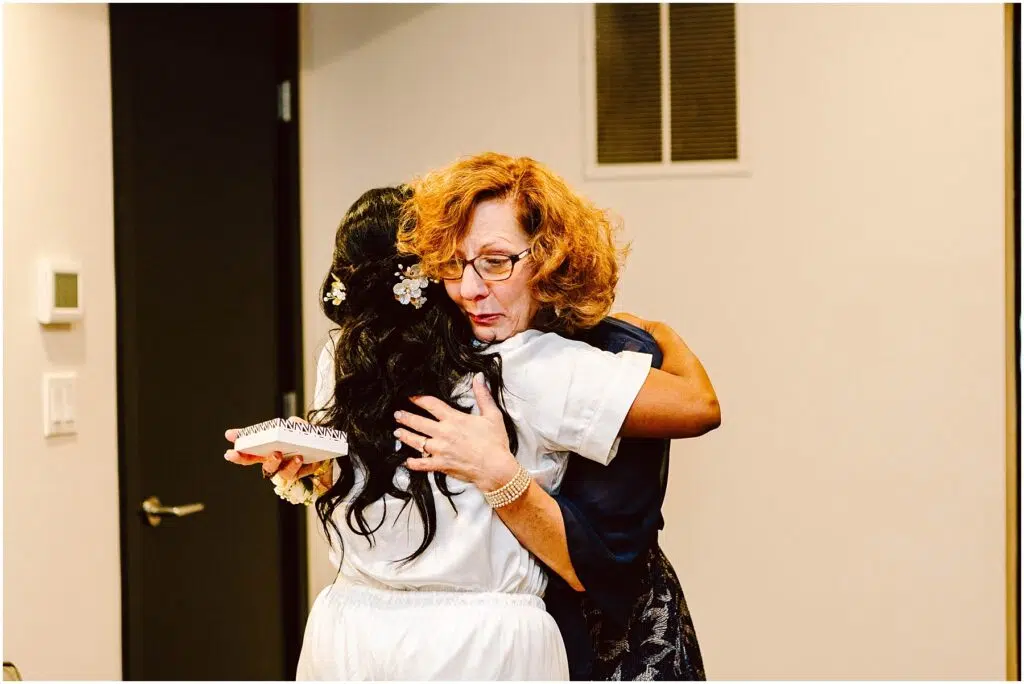 Snohomish Wedding Photographer GSquared Weddings A woman with curly red hair hugs another woman with long black hair and a floral hair accessory The woman being hugged holds a small white rectangular object They are standing in a room with beige walls and a black door Serving Seattle Snohomish and Washington State Snohomish Wedding Photographer GSquared Weddings A woman with curly red hair hugs another woman with long black hair and a floral hair accessory. The woman being hugged holds a small, white, rectangular object. They are standing in a room with beige walls and a black door. Serving Seattle, Snohomish and Washington State