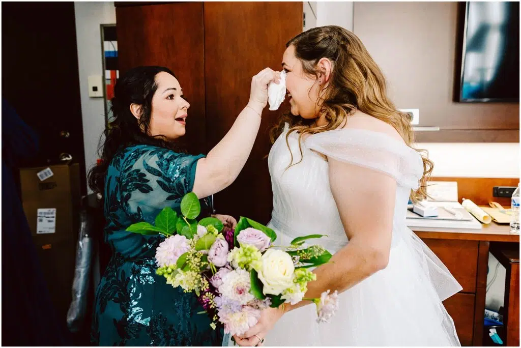 Snohomish Wedding Photographer GSquared Weddings A woman in a white wedding dress holds a bouquet of flowers while another woman in a teal dress gently dabs her face with a tissue They are in a room with wooden cabinets and soft lighting Serving Seattle Snohomish and Washington State Snohomish Wedding Photographer GSquared Weddings A woman in a white wedding dress holds a bouquet of flowers while another woman, in a teal dress, gently dabs her face with a tissue. They are in a room with wooden cabinets and soft lighting. Serving Seattle, Snohomish and Washington State