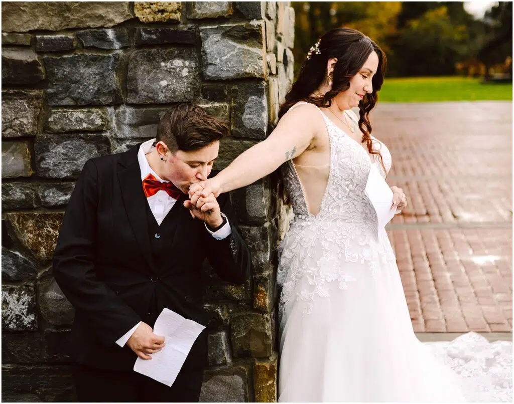 Snohomish Wedding Photographer GSquared Weddings A person in a suit and red bow tie kisses the hand of a person in a white wedding dress Both hold pieces of paper and stand near a stone wall outdoors on a brick pathway Serving Seattle Snohomish and Washington State Snohomish Wedding Photographer GSquared Weddings A person in a suit and red bow tie kisses the hand of a person in a white wedding dress. Both hold pieces of paper and stand near a stone wall, outdoors on a brick pathway. Serving Seattle, Snohomish and Washington State