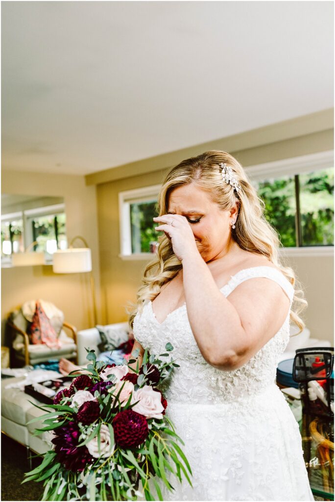 Snohomish wedding photographer gsquared weddings a bride in a white lace gown and floral hairpiece wipes tears from her eyes holding a bouquet with dark red and white flowers She stands in a brightly lit room with modern furniture and large windows Serving seattle snohomish and washington state Snohomish wedding photographer gsquared weddings a bride in a white lace gown and floral hairpiece wipes tears from her eyes holding a bouquet with dark red and white flowers She stands in a brightly lit room with modern furniture and large windows Serving seattle snohomish and washington state
