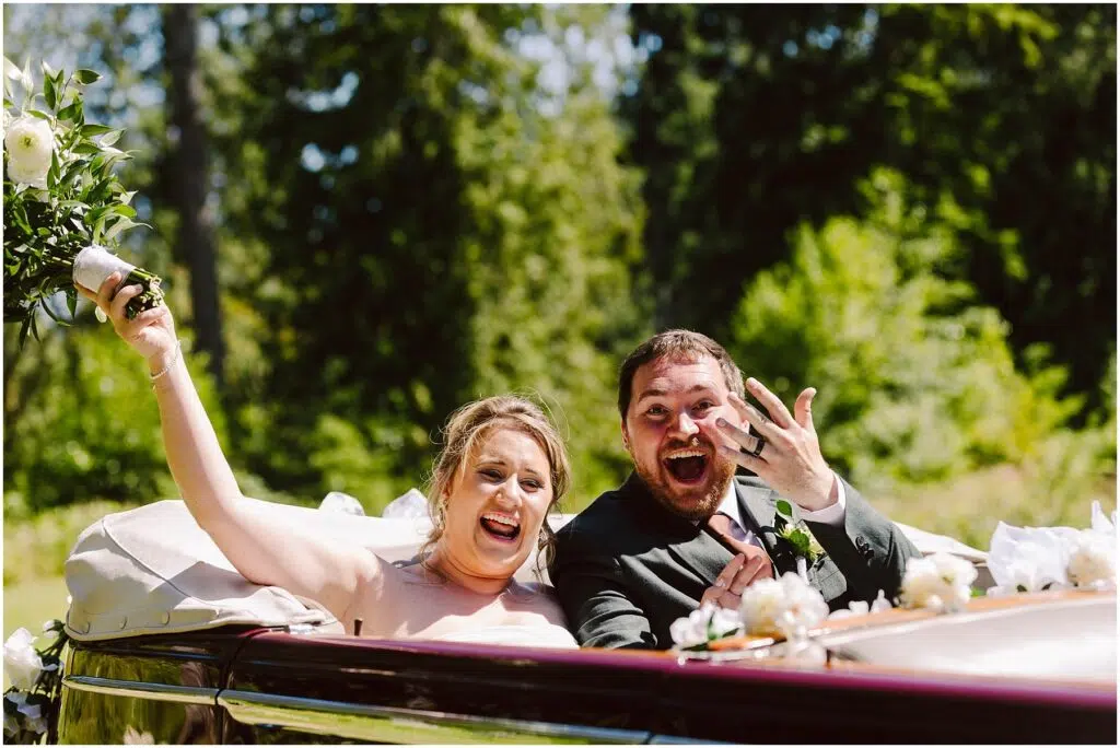 Snohomish Wedding Photographer GSquared Weddings A joyful bride and groom are sitting in a classic convertible The bride holds a bouquet aloft and the groom shows off his wedding ring Both are smiling widely against a backdrop of lush green trees Serving Seattle Snohomish and Washington State Snohomish Wedding Photographer GSquared Weddings A joyful bride and groom are sitting in a classic convertible. The bride holds a bouquet aloft and the groom shows off his wedding ring. Both are smiling widely against a backdrop of lush green trees. Serving Seattle, Snohomish and Washington State