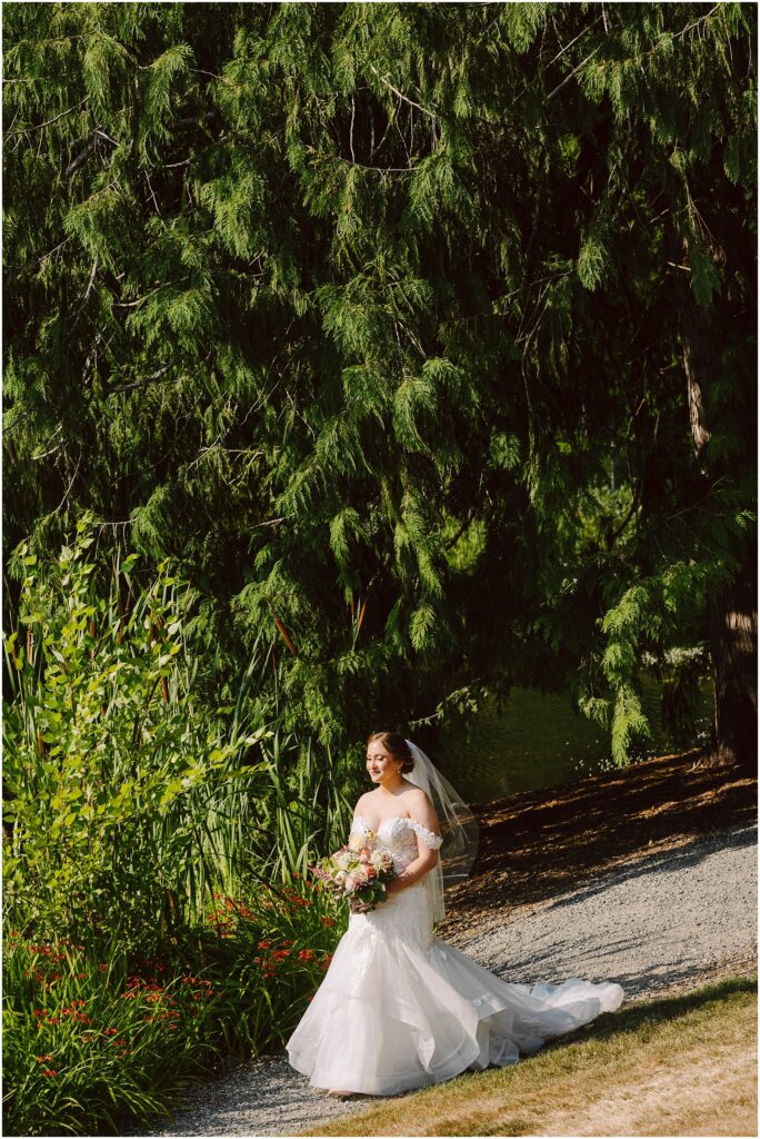 Snohomish Wedding Photographer GSquared Weddings A bride in a white wedding dress and veil walks on a gravel path holding a bouquet of flowers She is surrounded by lush green trees and plants with sunlight filtering through the leaves creating a serene outdoor setting Serving Seattle Snohomish and Washington State Snohomish Wedding Photographer GSquared Weddings A bride in a white wedding dress and veil walks on a gravel path, holding a bouquet of flowers. She is surrounded by lush green trees and plants, with sunlight filtering through the leaves, creating a serene outdoor setting. Serving Seattle, Snohomish and Washington State