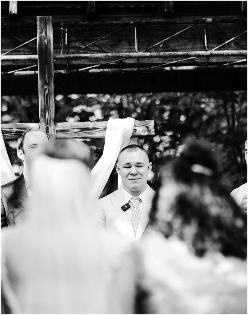 Snohomish Wedding Photographer GSquared Weddings Groom in a light suit stands in front of a wooden cross with white drapery at an outdoor wedding ceremony looking towards the bride and guests Serving Seattle Snohomish and Washington State Snohomish Wedding Photographer GSquared Weddings Groom in a light suit stands in front of a wooden cross with white drapery at an outdoor wedding ceremony, looking towards the bride and guests. Serving Seattle, Snohomish and Washington State