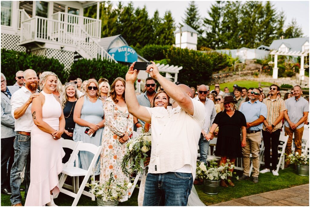 Snohomish Wedding Photographer GSquared Weddings A group of people gathered outdoors posing for a selfie taken by a man in a white shirt They are smiling and standing among white chairs surrounded by greenery and a building in the background Serving Seattle Snohomish and Washington State Snohomish Wedding Photographer GSquared Weddings A group of people gathered outdoors, posing for a selfie taken by a man in a white shirt. They are smiling and standing among white chairs, surrounded by greenery and a building in the background. Serving Seattle, Snohomish and Washington State