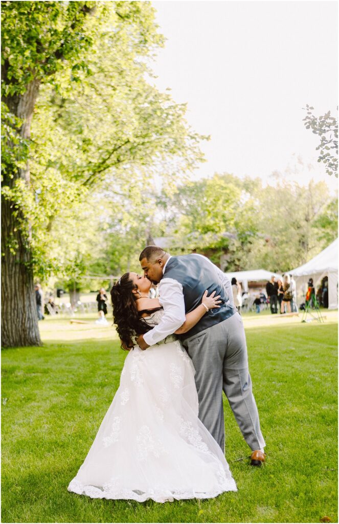 Snohomish wedding photographer gsquared weddings a bride and groom share a kiss while dancing on a grassy lawn The bride wears a white dress and the groom is in a suit with a vest Trees and a white tent are in the background on a sunny day Serving seattle snohomish and washington state