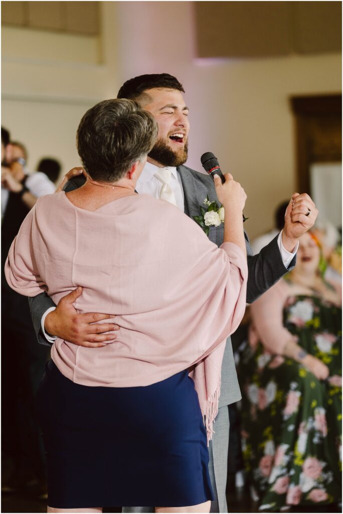 Snohomish wedding photographer gsquared weddings a groom in a gray suit and a woman in a pink shawl dance closely while both hold a microphone They appear to be singing or speaking together The background shows seated guests some in floral attire at a wedding reception Serving seattle snohomish and washington state