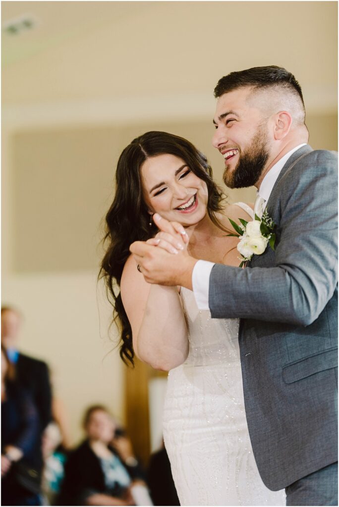 Snohomish wedding photographer gsquared weddings a bride and groom joyfully dance together smiling and holding hands The bride wears a white gown and the groom is in a gray suit with a boutonniere Blurred guests are visible in the background Serving seattle snohomish and washington state