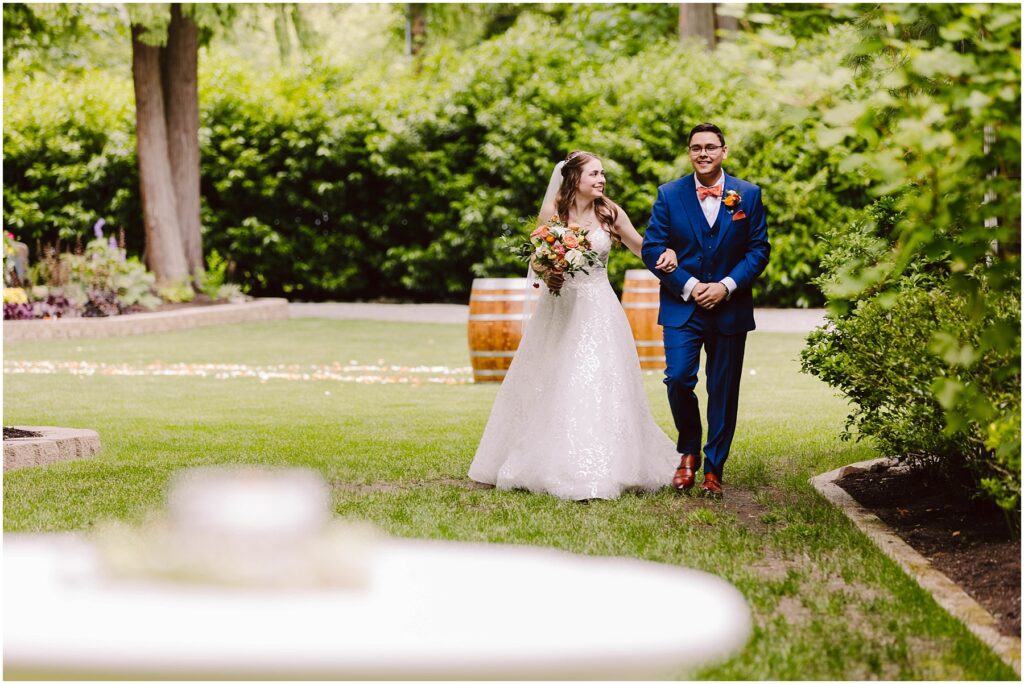Snohomish wedding photographer gsquared weddings a bride in a white gown and a groom in a blue suit walk joyfully through a lush garden She holds a colorful bouquet and there are wooden barrels in the background The scene is bright and surrounded by greenery Serving seattle snohomish and washington state