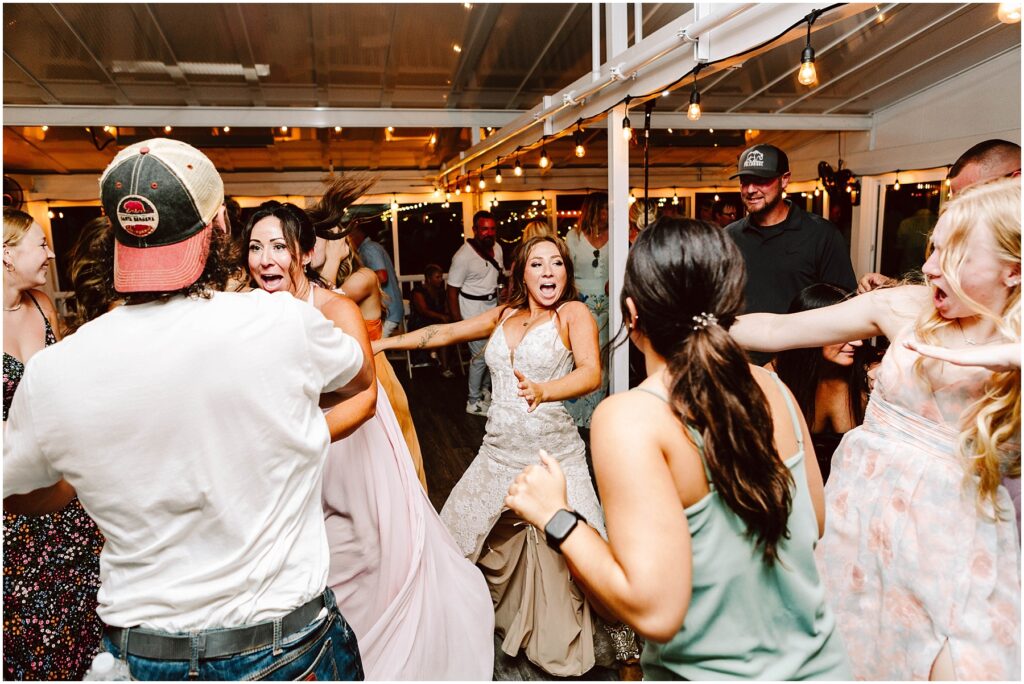 Snohomish wedding photographer gsquared weddings a lively wedding reception with a bride in a white dress energetically dancing among guests People around her are laughing and moving joyfully String lights illuminate the festive atmosphere Serving seattle snohomish and washington state