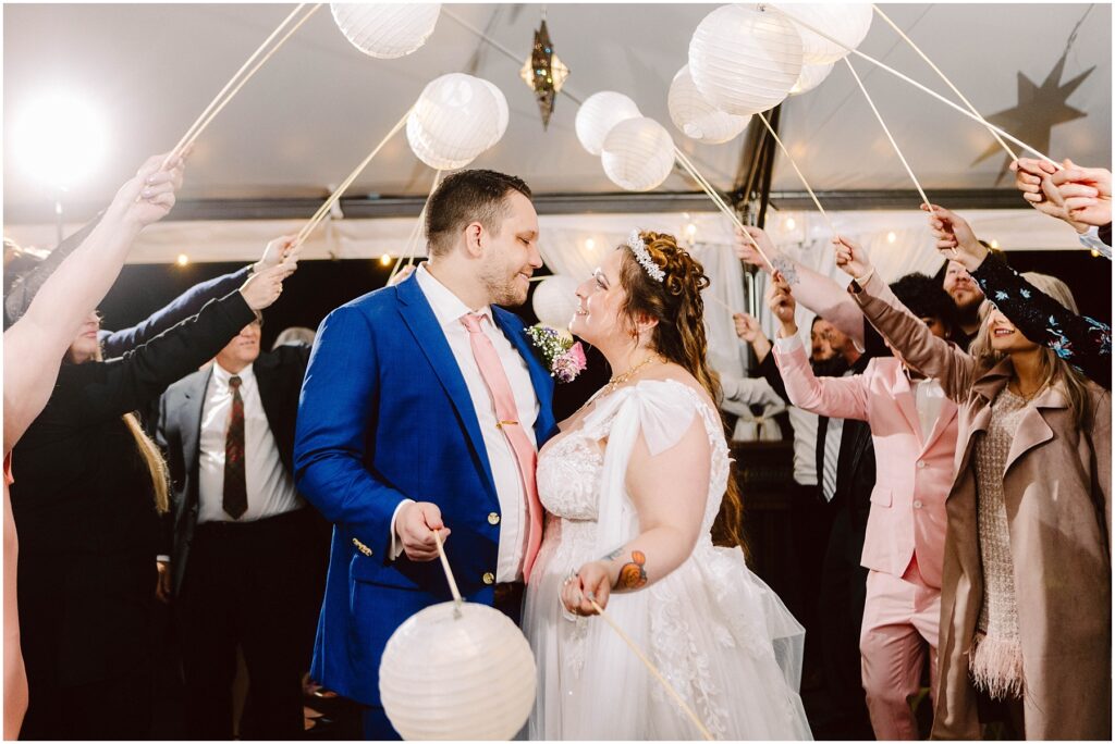 Snohomish wedding photographer gsquared weddings a bride and groom smiling at each other under a canopy of white paper lanterns held by guests The groom wears a blue suit and pink tie while the bride is in a white dress Some guests are dressed in suits and dresses The setting is festive and joyful Serving seattle snohomish and washington state