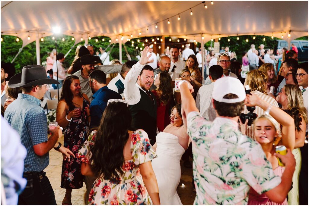 Snohomish wedding photographer gsquared weddings a lively wedding reception under a tent with string lights Guests are dancing energetically with one person lifting their arm in celebration The crowd includes people in festive attire capturing the joyful atmosphere Serving seattle snohomish and washington state