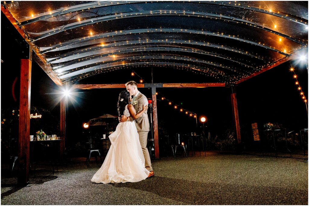 Snohomish wedding photographer gsquared weddings a bride and groom share their first dance under a canopy adorned with string lights at night The bride wears a flowing white dress and the groom is in a light gray suit The setting is romantic with a dimly lit intimate atmosphere Serving seattle snohomish and washington state