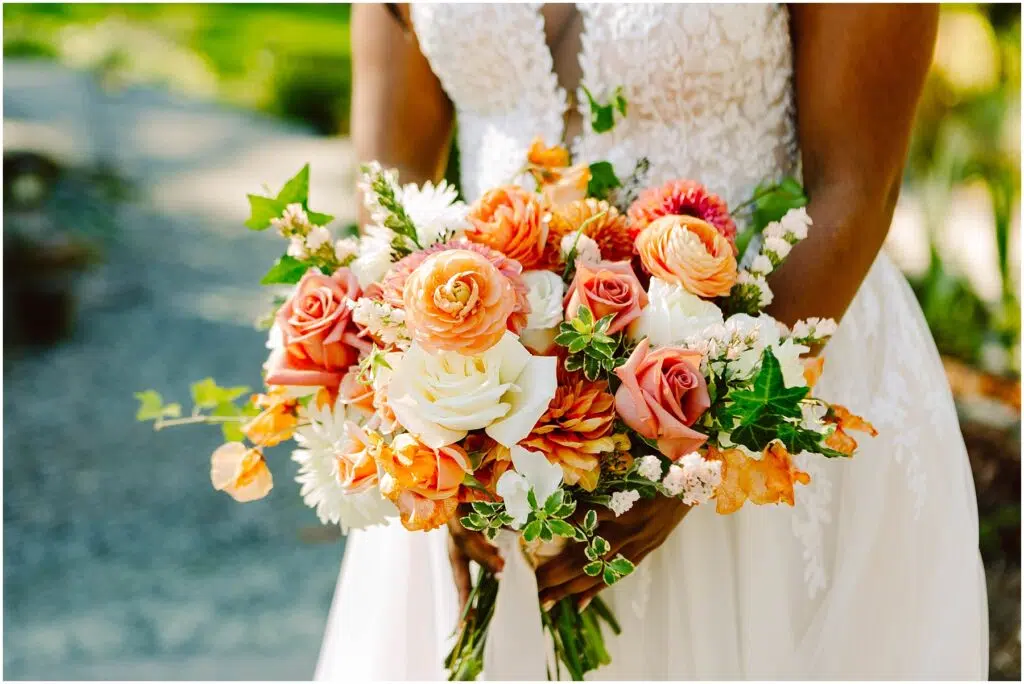 Snohomish Wedding Photographer GSquared Weddings A bride holds a vibrant bouquet of orange pink and white flowers mixed with greenery She wears a white lace dress The background is a blurred outdoor scene with green foliage Serving Seattle Snohomish and Washington State Snohomish Wedding Photographer GSquared Weddings A bride holds a vibrant bouquet of orange, pink, and white flowers mixed with greenery. She wears a white lace dress. The background is a blurred outdoor scene with green foliage. Serving Seattle, Snohomish and Washington State