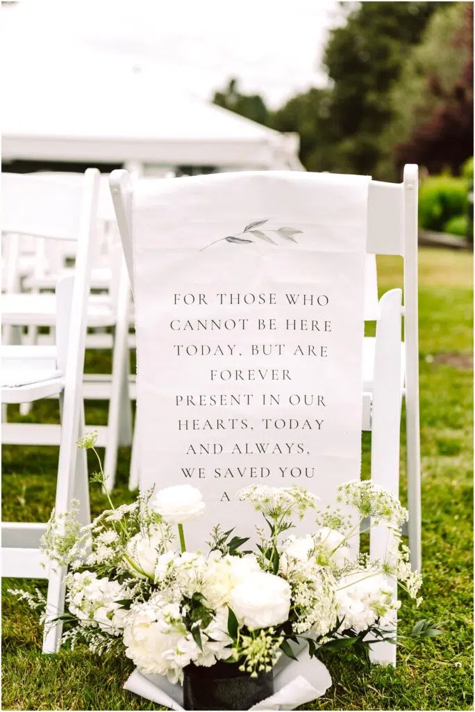 Snohomish Wedding Photographer GSquared Weddings A white chair on grass holds a sign with a heartfelt message about absent loved ones adorned with floral designs In front of the chair theres a bouquet of white flowers and greenery More chairs and a tent are visible in the background Serving Seattle Snohomish and Washington State Snohomish Wedding Photographer GSquared Weddings A white chair on grass holds a sign with a heartfelt message about absent loved ones, adorned with floral designs. In front of the chair, theres a bouquet of white flowers and greenery. More chairs and a tent are visible in the background. Serving Seattle, Snohomish and Washington State