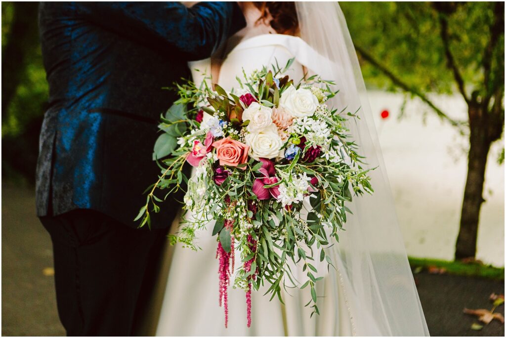 Snohomish wedding photographer gsquared weddings bride holding a large vibrant bouquet of pink white and purple flowers with green foliage She stands beside a person in a dark suit Background shows trees and a white surface possibly a building or wall Serving seattle snohomish and washington state Snohomish wedding photographer gsquared weddings bride holding a large vibrant bouquet of pink white and purple flowers with green foliage She stands beside a person in a dark suit Background shows trees and a white surface possibly a building or wall Serving seattle snohomish and washington state