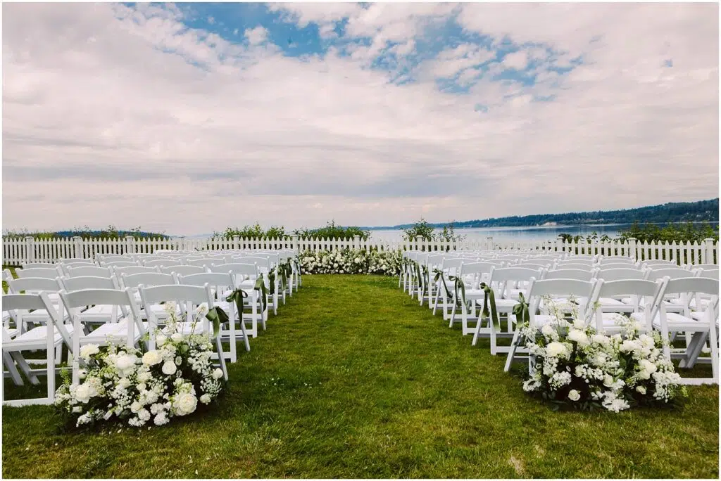 Snohomish Wedding Photographer GSquared Weddings A scenic outdoor wedding setup features two rows of white chairs lined with white floral arrangements on a grassy area A white picket fence overlooks a body of water and a cloudy sky providing a picturesque backdrop Serving Seattle Snohomish and Washington State Snohomish Wedding Photographer GSquared Weddings A scenic outdoor wedding setup features two rows of white chairs lined with white floral arrangements on a grassy area. A white picket fence overlooks a body of water and a cloudy sky, providing a picturesque backdrop. Serving Seattle, Snohomish and Washington State