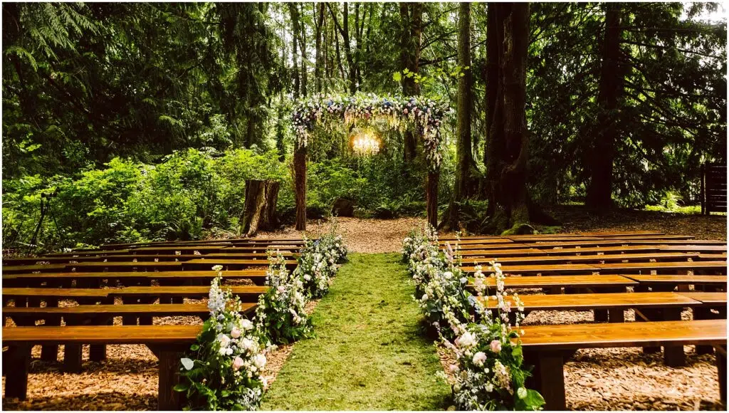 Snohomish Wedding Photographer GSquared Weddings A serene outdoor wedding setup in a forest Wooden benches line a grassy aisle adorned with floral arrangements An arch decorated with flowers stands at the end surrounded by lush green trees and soft sunlight filtering through the leaves Serving Seattle Snohomish and Washington State Snohomish Wedding Photographer GSquared Weddings A serene outdoor wedding setup in a forest. Wooden benches line a grassy aisle adorned with floral arrangements. An arch decorated with flowers stands at the end, surrounded by lush green trees and soft sunlight filtering through the leaves. Serving Seattle, Snohomish and Washington State
