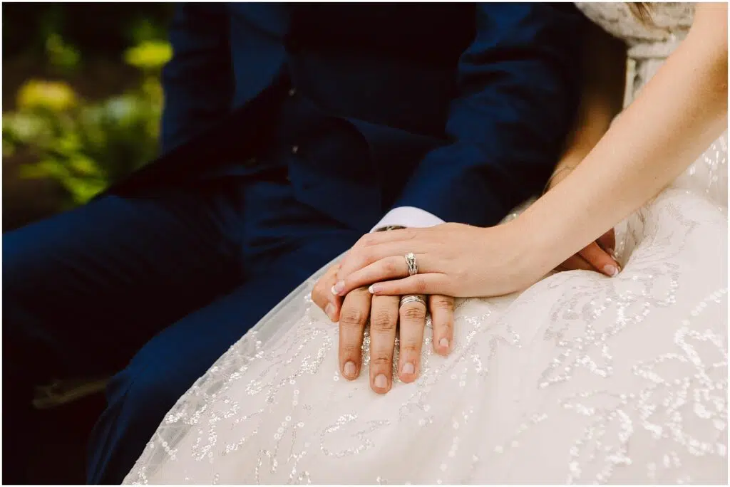 Snohomish Wedding Photographer GSquared Weddings Closeup of a couple sitting holding hands The person on the left is wearing a dark blue suit and the person on the right is in a white sequined dress with a wedding ring visible The background is softly blurred with greenery Serving Seattle Snohomish and Washington State Snohomish Wedding Photographer GSquared Weddings Close-up of a couple sitting, holding hands. The person on the left is wearing a dark blue suit, and the person on the right is in a white, sequined dress with a wedding ring visible. The background is softly blurred with greenery. Serving Seattle, Snohomish and Washington State