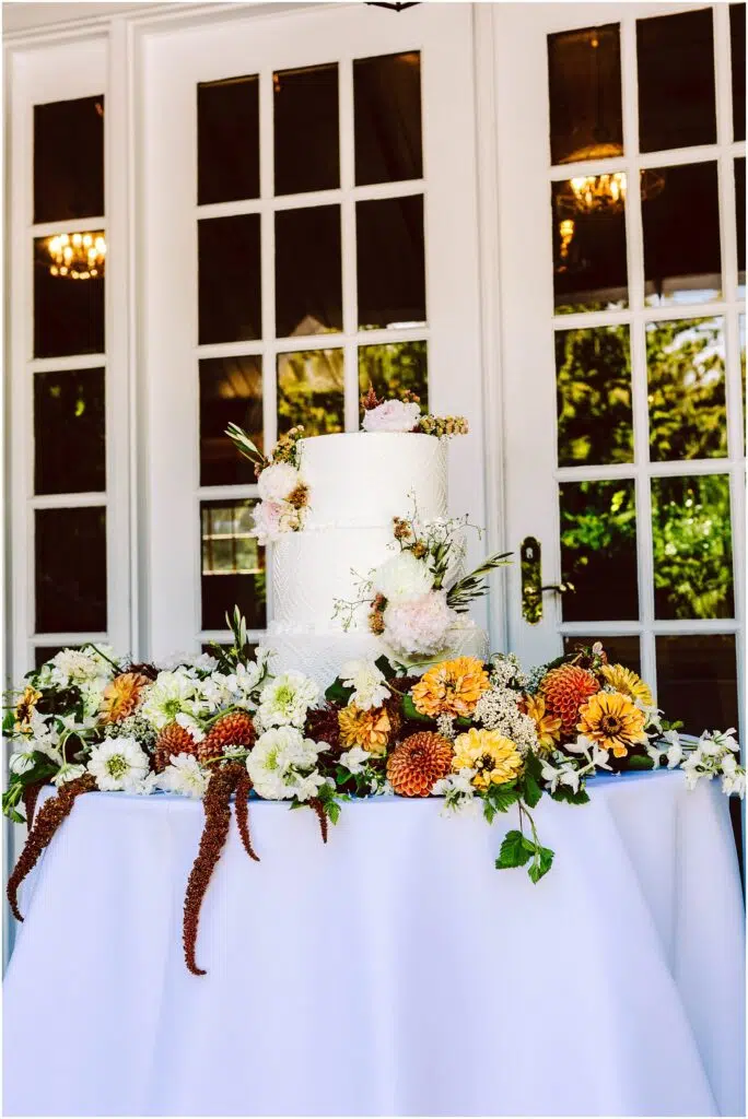 Snohomish Wedding Photographer GSquared Weddings A white twotier wedding cake adorned with pink and white flowers sits on a table covered with a white cloth The table is decorated with a variety of colorful flowers and greenery against a backdrop of white French doors with glass panes Serving Seattle Snohomish and Washington State Snohomish Wedding Photographer GSquared Weddings A white, two-tier wedding cake adorned with pink and white flowers sits on a table covered with a white cloth. The table is decorated with a variety of colorful flowers and greenery, against a backdrop of white French doors with glass panes. Serving Seattle, Snohomish and Washington State