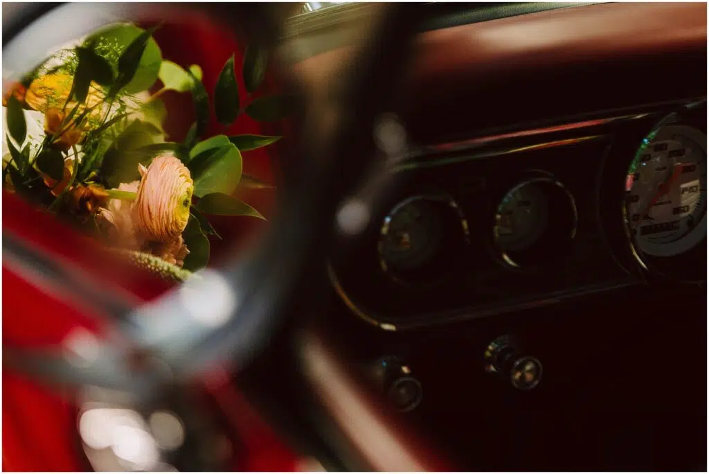 Snohomish Wedding Photographer GSquared Weddings Closeup of a car interior focusing on the dashboard with instruments and knobs visible A reflection in the side mirror shows a bouquet with pink and yellow flowers and green leaves The image has a warm vintage feel Serving Seattle Snohomish and Washington State Snohomish Wedding Photographer GSquared Weddings Close-up of a car interior, focusing on the dashboard with instruments and knobs visible. A reflection in the side mirror shows a bouquet with pink and yellow flowers and green leaves. The image has a warm, vintage feel. Serving Seattle, Snohomish and Washington State