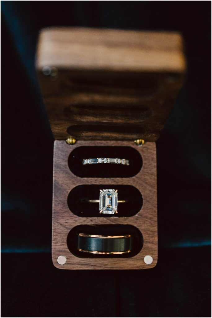 Snohomish wedding photographer gsquared weddings a wooden box with three compartments holds an emerald-cut diamond ring a thin diamond-studded band and a solid band possibly a wedding ring set The box is open displaying the rings against a dark background Serving seattle snohomish and washington state Snohomish wedding photographer gsquared weddings a wooden box with three compartments holds an emerald cut diamond ring a thin diamond studded band and a solid band possibly a wedding ring set The box is open displaying the rings against a dark background Serving seattle snohomish and washington state