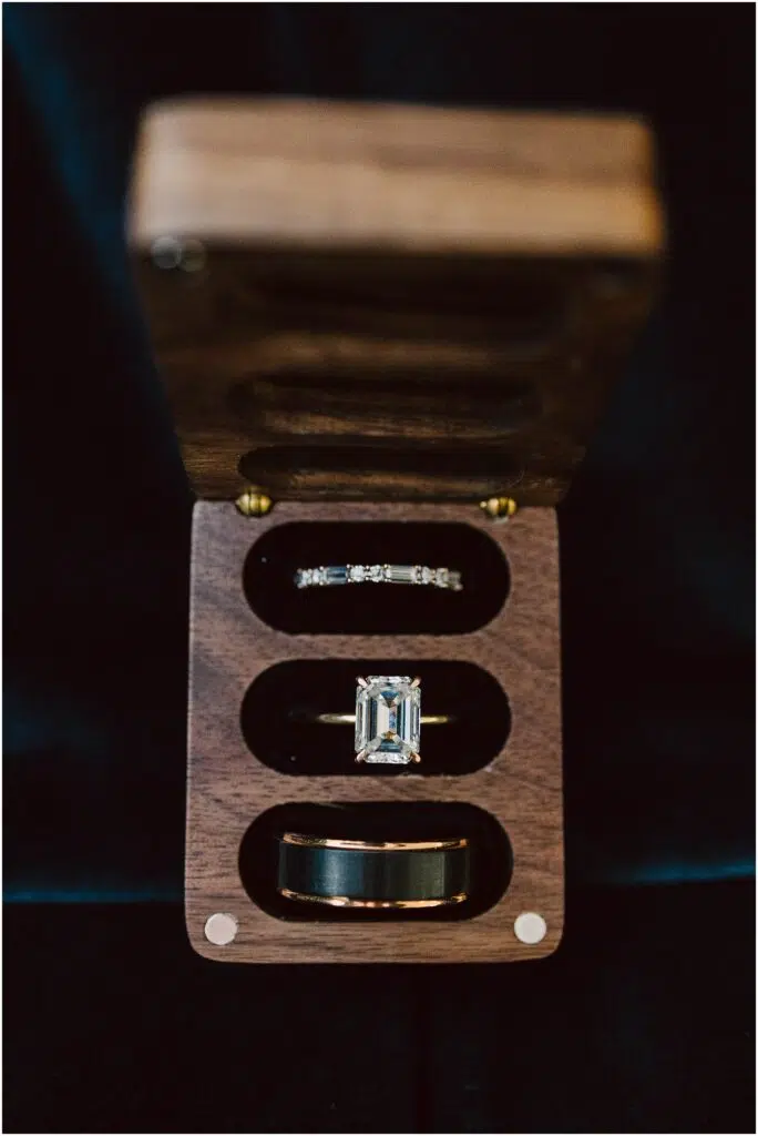 Snohomish Wedding Photographer GSquared Weddings A wooden box with three compartments holds an emeraldcut diamond ring a thin diamondstudded band and a solid band possibly a wedding ring set The box is open displaying the rings against a dark background Serving Seattle Snohomish and Washington State Snohomish Wedding Photographer GSquared Weddings A wooden box with three compartments holds an emerald-cut diamond ring, a thin diamond-studded band, and a solid band, possibly a wedding ring set. The box is open, displaying the rings against a dark background. Serving Seattle, Snohomish and Washington State