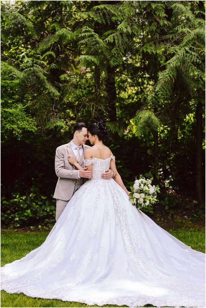 Snohomish wedding photographer gsquared weddings a couple stands in a lush garden embracing under tall trees The bride wears an elegant white gown holding a bouquet of flowers The groom is in a light-colored suit They share a tender moment facing each other closely Serving seattle snohomish and washington state Snohomish wedding photographer gsquared weddings a couple stands in a lush garden embracing under tall trees The bride wears an elegant white gown holding a bouquet of flowers The groom is in a light colored suit They share a tender moment facing each other closely Serving seattle snohomish and washington state