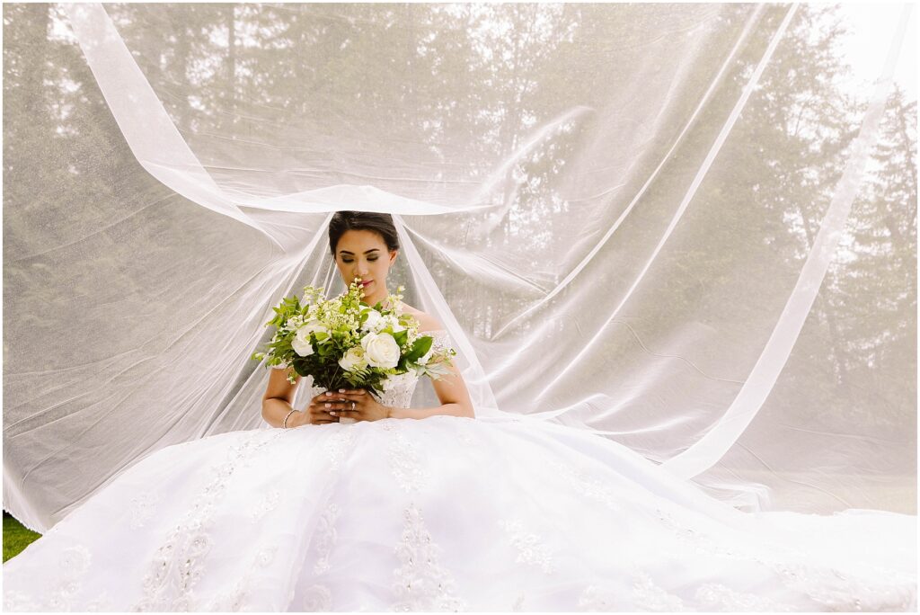 Snohomish wedding photographer gsquared weddings a bride in an elegant white gown sits holding a bouquet of white and green flowers Her veil is spread out behind her creating a delicate backdrop The scene is set outdoors with a blurred background of trees Serving seattle snohomish and washington state Snohomish wedding photographer gsquared weddings a bride in an elegant white gown sits holding a bouquet of white and green flowers Her veil is spread out behind her creating a delicate backdrop The scene is set outdoors with a blurred background of trees Serving seattle snohomish and washington state