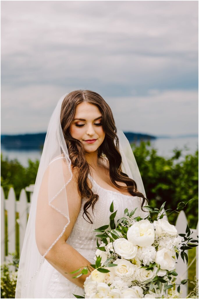 Snohomish wedding photographer gsquared weddings a bride stands outdoors with a white picket fence and waterfront view in the background She holds a bouquet of white flowers and greenery wearing a white dress and veil The sky is overcast Serving seattle snohomish and washington state Snohomish wedding photographer gsquared weddings a bride stands outdoors with a white picket fence and waterfront view in the background She holds a bouquet of white flowers and greenery wearing a white dress and veil The sky is overcast Serving seattle snohomish and washington state