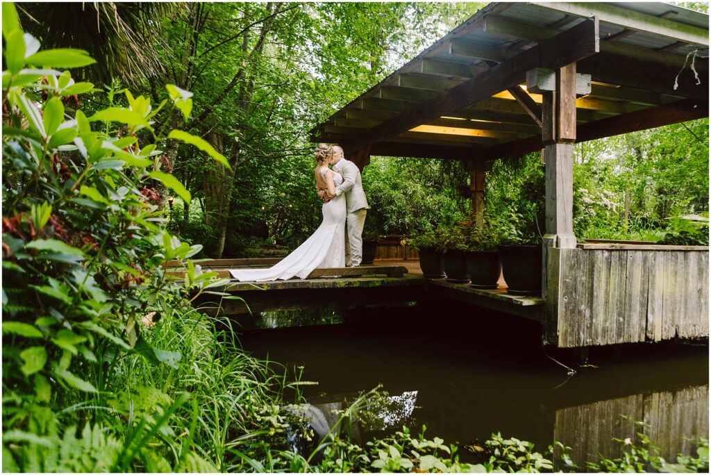 Snohomish wedding photographer gsquared weddings a couple in wedding attire embraces under a wooden gazebo surrounded by lush greenery A small pond with reflective water is in the foreground adding to the serene and romantic setting Serving seattle snohomish and washington state Snohomish wedding photographer gsquared weddings a couple in wedding attire embraces under a wooden gazebo surrounded by lush greenery A small pond with reflective water is in the foreground adding to the serene and romantic setting Serving seattle snohomish and washington state