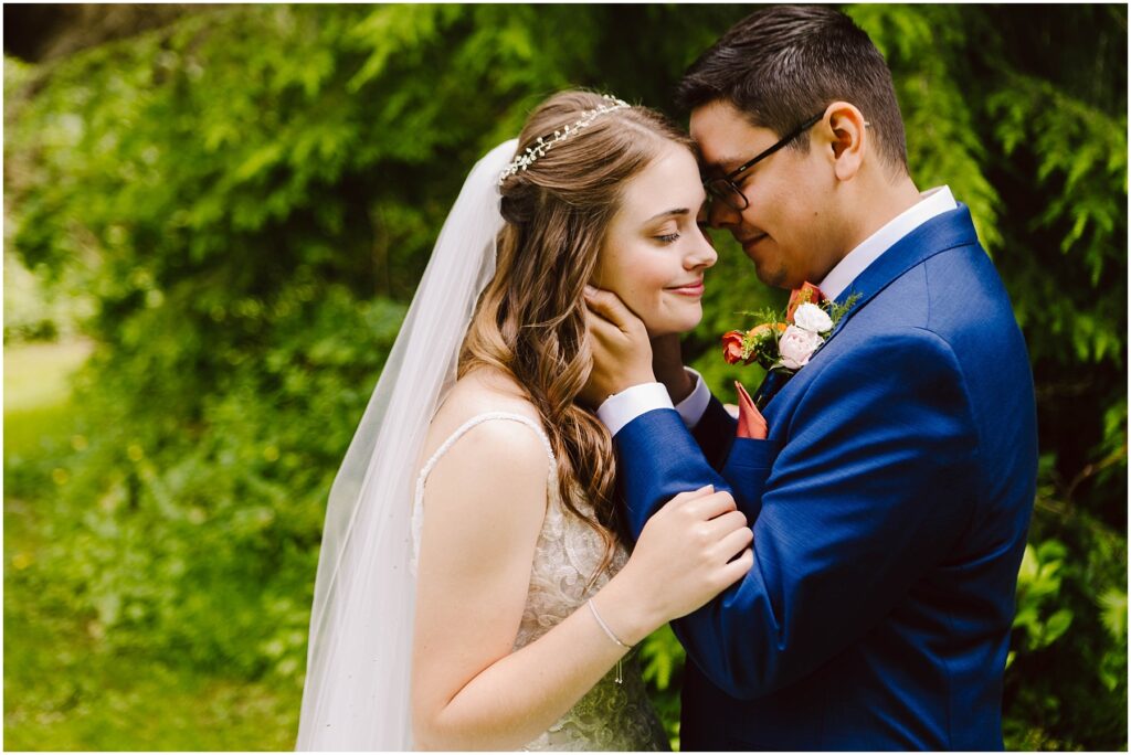 Snohomish wedding photographer gsquared weddings a bride in a white gown and veil and a groom in a blue suit share a tender moment outdoors The groom gently touches the brides face as they both smile with their eyes closed surrounded by lush greenery Serving seattle snohomish and washington state Snohomish wedding photographer gsquared weddings a bride in a white gown and veil and a groom in a blue suit share a tender moment outdoors The groom gently touches the brides face as they both smile with their eyes closed surrounded by lush greenery Serving seattle snohomish and washington state