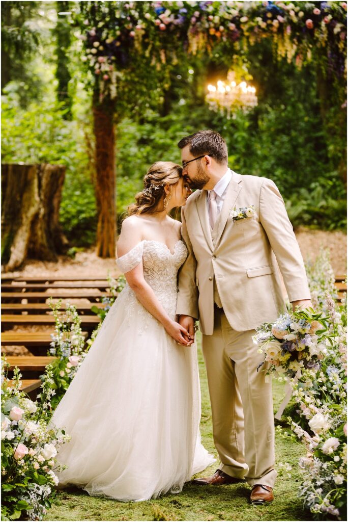 Snohomish wedding photographer gsquared weddings a bride and groom hold hands and lean in for a kiss in an outdoor wedding setting The bride wears an off-shoulder gown and the groom dons a beige suit They are surrounded by greenery and floral arrangements with a chandelier hanging above Serving seattle snohomish and washington state Snohomish wedding photographer gsquared weddings a bride and groom hold hands and lean in for a kiss in an outdoor wedding setting The bride wears an off shoulder gown and the groom dons a beige suit They are surrounded by greenery and floral arrangements with a chandelier hanging above Serving seattle snohomish and washington state