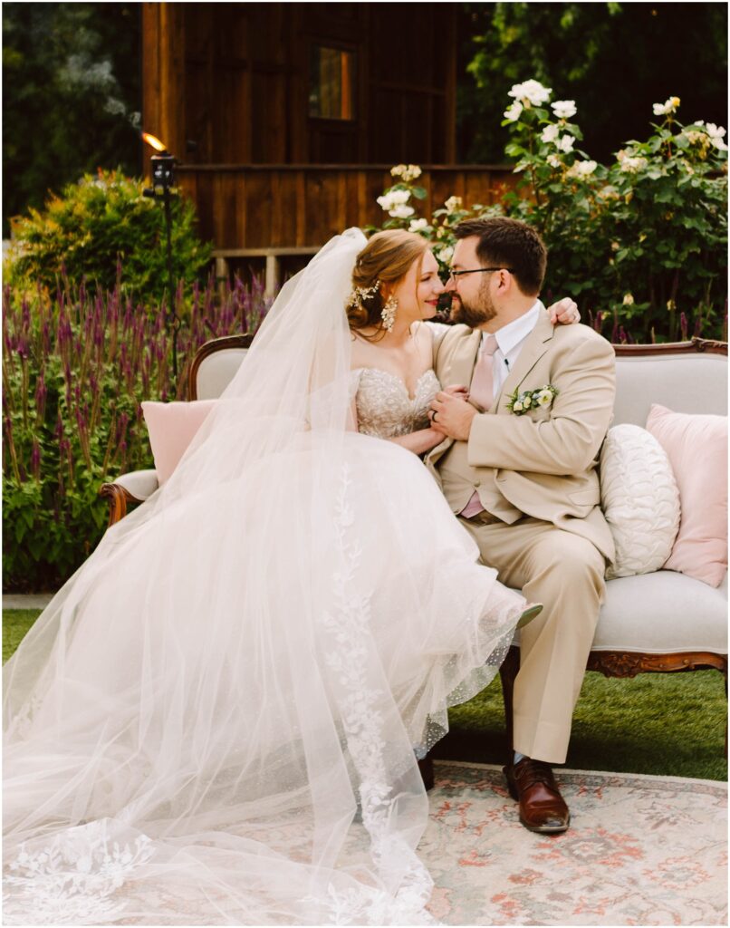 Snohomish wedding photographer gsquared weddings a bride and groom sit closely on an outdoor sofa surrounded by flowers The bride wears a white dress with a long veil and the groom wears a tan suit They gaze into each others eyes holding hands with a wooden building in the background Serving seattle snohomish and washington state Snohomish wedding photographer gsquared weddings a bride and groom sit closely on an outdoor sofa surrounded by flowers The bride wears a white dress with a long veil and the groom wears a tan suit They gaze into each others eyes holding hands with a wooden building in the background Serving seattle snohomish and washington state