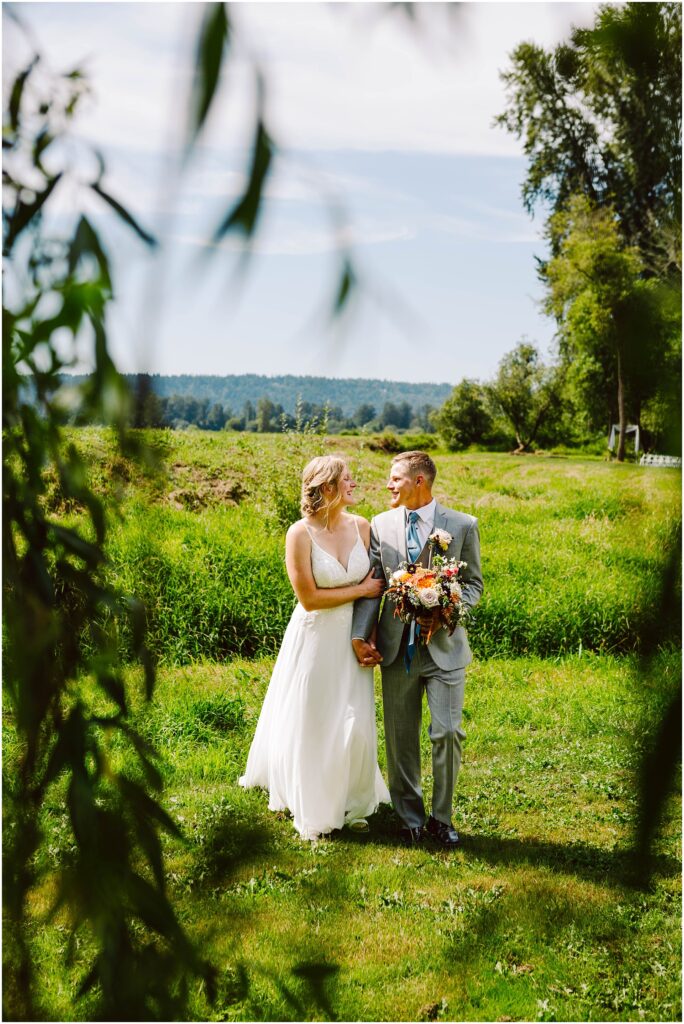 Snohomish wedding photographer gsquared weddings a couple stands in a lush green outdoor setting The woman wears a white dress and the man a gray suit They hold hands and smile at each other with flowers in their hands Trees and a clear blue sky are in the background Serving seattle snohomish and washington state Snohomish wedding photographer gsquared weddings a couple stands in a lush green outdoor setting The woman wears a white dress and the man a gray suit They hold hands and smile at each other with flowers in their hands Trees and a clear blue sky are in the background Serving seattle snohomish and washington state