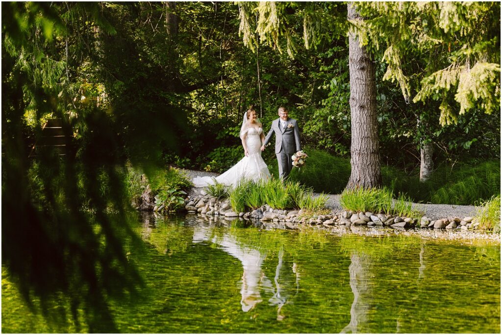 Snohomish wedding photographer gsquared weddings a bride in a white gown and a groom in a gray suit walk hand in hand on a path beside a serene green pond surrounded by lush trees and vegetation Their reflection is visible in the water Serving seattle snohomish and washington state Snohomish wedding photographer gsquared weddings a bride in a white gown and a groom in a gray suit walk hand in hand on a path beside a serene green pond surrounded by lush trees and vegetation Their reflection is visible in the water Serving seattle snohomish and washington state