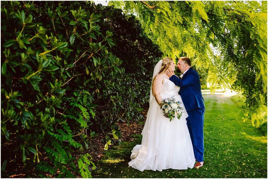 Snohomish wedding photographer gsquared weddings a bride in a white gown and veil holding a bouquet of blue and white flowers gazes lovingly at a groom in a blue suit They stand close under lush green trees with sunlight filtering through the leaves creating a romantic serene setting Serving seattle snohomish and washington state Snohomish wedding photographer gsquared weddings a bride in a white gown and veil holding a bouquet of blue and white flowers gazes lovingly at a groom in a blue suit They stand close under lush green trees with sunlight filtering through the leaves creating a romantic serene setting Serving seattle snohomish and washington state