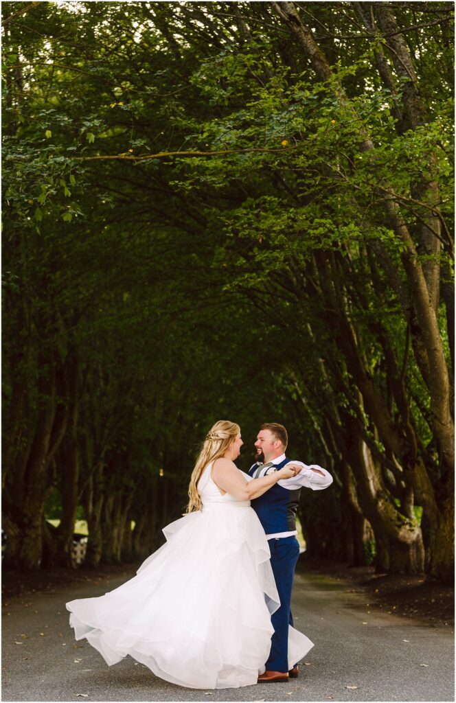 Snohomish wedding photographer gsquared weddings a couple dances on a road under a canopy of lush green trees The woman wears a flowing white gown and the man is in a blue suit They are surrounded by a serene verdant environment creating a romantic and whimsical atmosphere Serving seattle snohomish and washington state Snohomish wedding photographer gsquared weddings a couple dances on a road under a canopy of lush green trees The woman wears a flowing white gown and the man is in a blue suit They are surrounded by a serene verdant environment creating a romantic and whimsical atmosphere Serving seattle snohomish and washington state