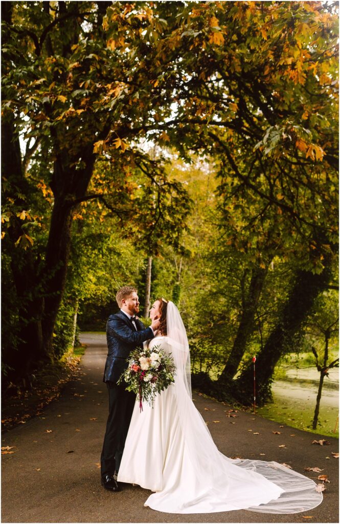 Snohomish wedding photographer gsquared weddings a couple in wedding attire embrace on a tree-lined path The bride wears a white gown and veil holding a bouquet while the groom is in a dark suit Autumn leaves add color to the scene with green and golden foliage overhead Serving seattle snohomish and washington state Snohomish wedding photographer gsquared weddings a couple in wedding attire embrace on a tree lined path The bride wears a white gown and veil holding a bouquet while the groom is in a dark suit Autumn leaves add color to the scene with green and golden foliage overhead Serving seattle snohomish and washington state