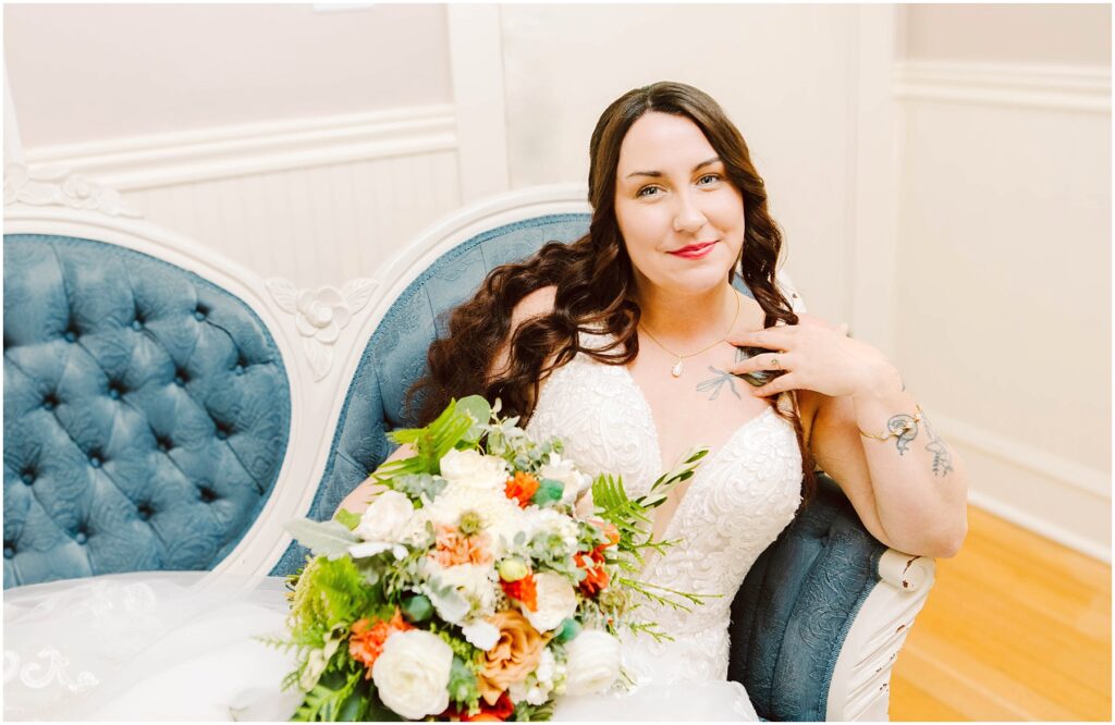 Snohomish wedding photographer gsquared weddings bride in a white lace wedding dress sits on a vintage blue couch holding a bouquet of white orange and green flowers She has long brown hair and is smiling softly with tattoos visible on her arms Serving seattle snohomish and washington state Snohomish wedding photographer gsquared weddings bride in a white lace wedding dress sits on a vintage blue couch holding a bouquet of white orange and green flowers She has long brown hair and is smiling softly with tattoos visible on her arms Serving seattle snohomish and washington state