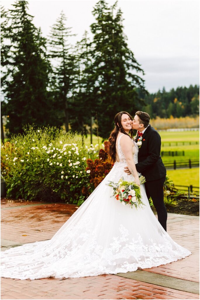 Snohomish wedding photographer gsquared weddings a bride in a white lace gown holds a bouquet while smiling as a person in a dark suit kisses her cheek They stand on a wet patio surrounded by greenery and trees The scene is outdoors on a cloudy day Serving seattle snohomish and washington state Snohomish wedding photographer gsquared weddings a bride in a white lace gown holds a bouquet while smiling as a person in a dark suit kisses her cheek They stand on a wet patio surrounded by greenery and trees The scene is outdoors on a cloudy day Serving seattle snohomish and washington state