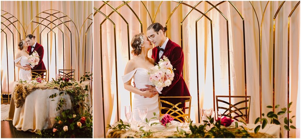 Snohomish Wedding Photographer GSquared Weddings A bride and groom embrace in front of a decorated table with floral arrangements. The groom wears a red velvet suit, and the bride holds a bouquet. They stand beneath a gold arch, dressed in elegant wedding attire. Serving Seattle, Snohomish and Washington State