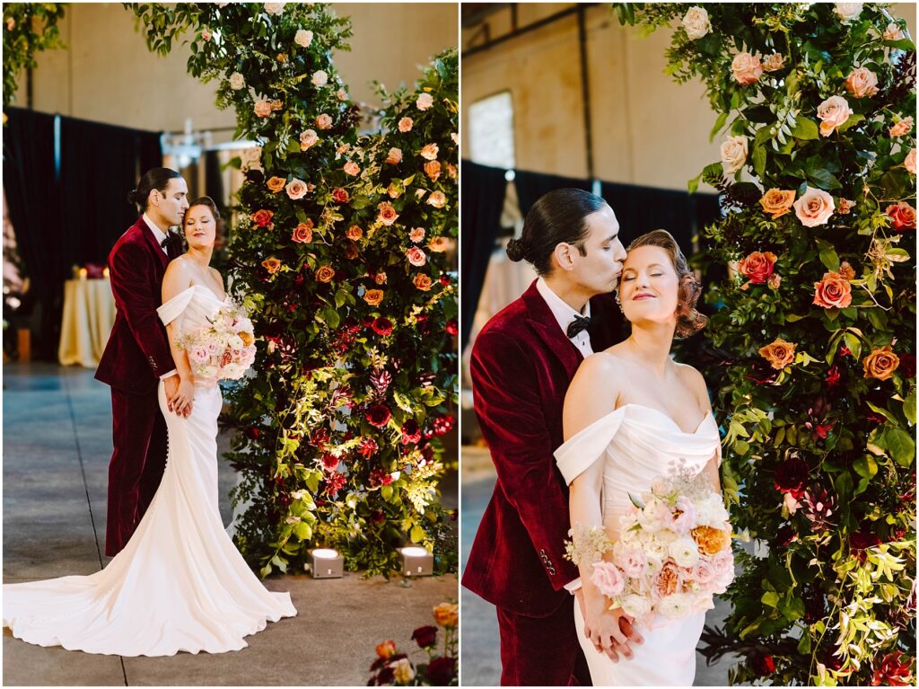Snohomish Wedding Photographer GSquared Weddings A couple stands together in an elegant setting. The person in a white gown holds a bouquet of flowers, while the person in a burgundy suit embraces them. They are surrounded by a floral arch with various blossoms. Serving Seattle, Snohomish and Washington State