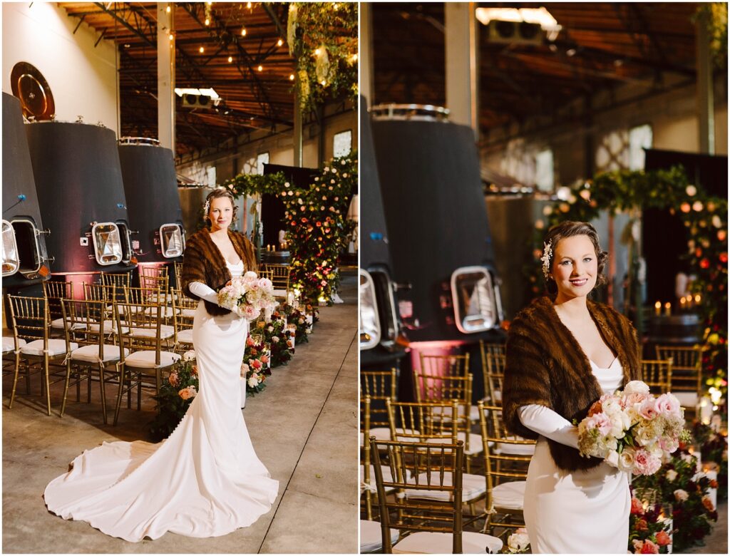 Snohomish Wedding Photographer GSquared Weddings A bride stands in an elegant industrial venue wearing a white gown and fur shawl, holding a bouquet of pink and white flowers. The aisle is lined with gold chairs and floral arrangements. The ceiling is adorned with greenery. Serving Seattle, Snohomish and Washington State