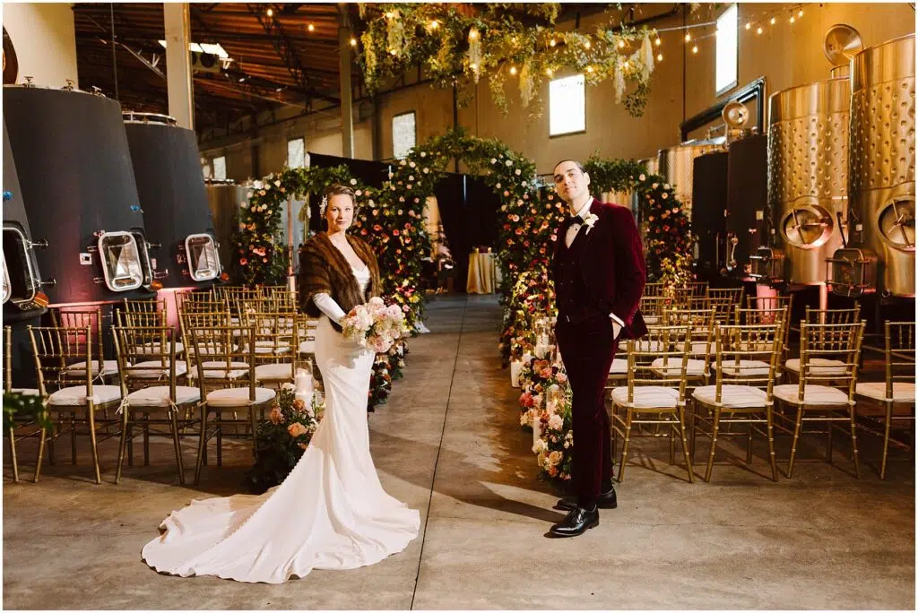 Snohomish Wedding Photographer GSquared Weddings A bride and groom stand in the center of an aisle adorned with flowers in an industrialstyle venue She wears a white gown and fur wrap holding a bouquet He wears a burgundy suit Rows of gold chairs and string lights enhance the setting Serving Seattle Snohomish and Washington State Snohomish Wedding Photographer GSquared Weddings A bride and groom stand in the center of an aisle adorned with flowers in an industrial-style venue. She wears a white gown and fur wrap, holding a bouquet. He wears a burgundy suit. Rows of gold chairs and string lights enhance the setting. Serving Seattle, Snohomish and Washington State