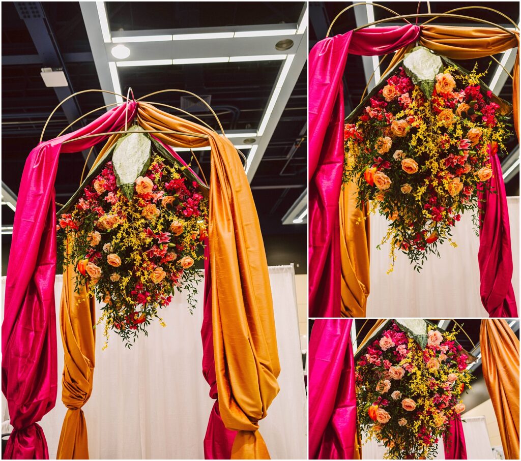 Snohomish Wedding Photographer GSquared Weddings A decorative archway draped with vibrant pink and orange fabric features a lush arrangement of yellow and pink flowers. The ceiling with white panels and lights is visible above the arch. Serving Seattle, Snohomish and Washington State