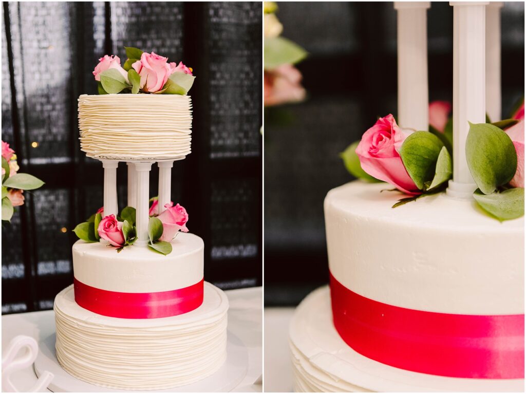 Snohomish Wedding Photographer GSquared Weddings Two-tier wedding cake with textured white frosting. The top tier is supported by pillars and adorned with pink roses and green leaves. A bright pink ribbon wraps around the base of each tier. Black backdrop with pink floral accents on the side. Serving Seattle, Snohomish and Washington State