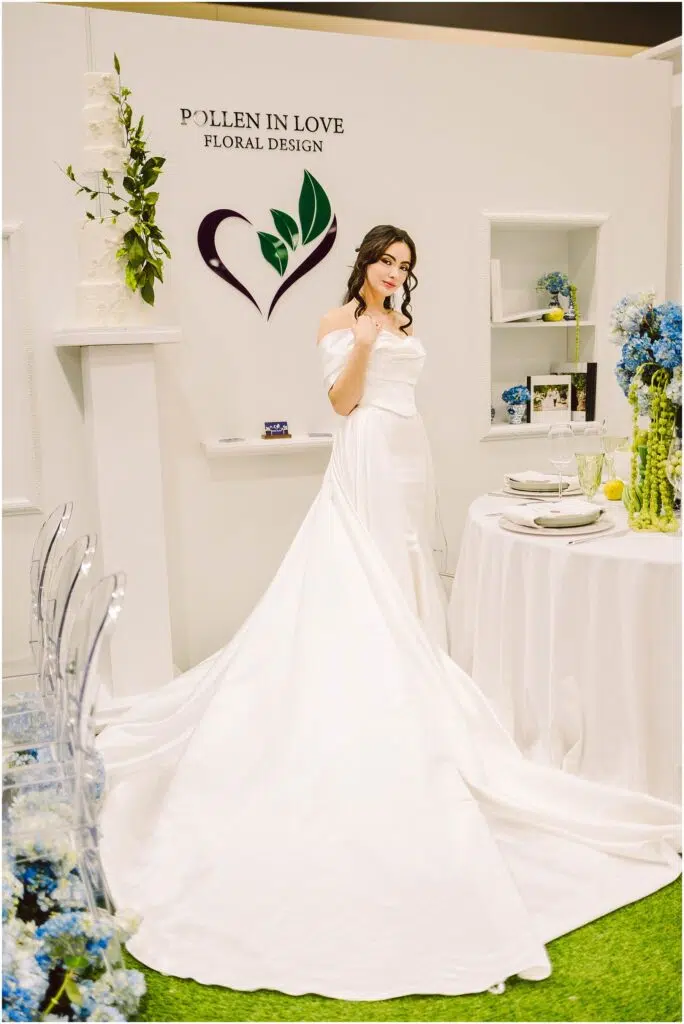 Snohomish Wedding Photographer GSquared Weddings A woman in a white wedding dress poses in front of a Pollen in Love Floral Design sign The setting includes a table with blue flowers elegant tableware and a long train extending from the dress The space has a sophisticated floral theme Serving Seattle Snohomish and Washington State Snohomish Wedding Photographer GSquared Weddings A woman in a white wedding dress poses in front of a Pollen in Love Floral Design sign. The setting includes a table with blue flowers, elegant tableware, and a long train extending from the dress. The space has a sophisticated floral theme. Serving Seattle, Snohomish and Washington State