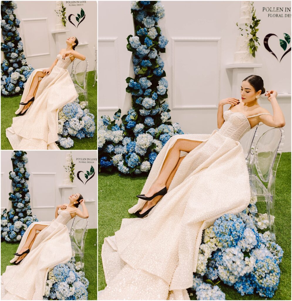 Snohomish Wedding Photographer GSquared Weddings A woman in a shimmering white gown with a high slit poses on a clear chair. The background features blue hydrangeas and white flowers against a white wall with two hearts. Grass covers the floor, creating a fresh, elegant scene. Serving Seattle, Snohomish and Washington State