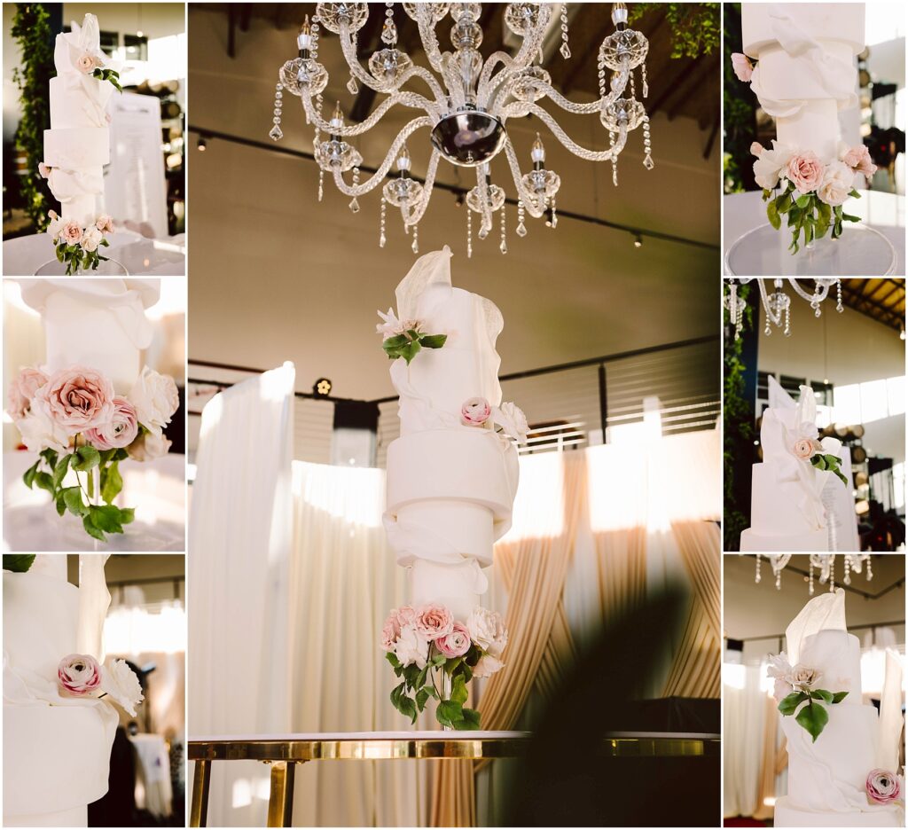 Snohomish Wedding Photographer GSquared Weddings A multi-tiered white wedding cake with elaborate swirling fondant designs, adorned with pink roses. The cake is displayed on a reflective table beneath a sparkling crystal chandelier, surrounded by draped curtains. Serving Seattle, Snohomish and Washington State